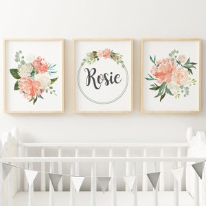 May include: Three framed prints with a floral theme. The center print features a wreath of flowers with the name "Rosie" in the center. The prints on either side feature bouquets of pink and white flowers.