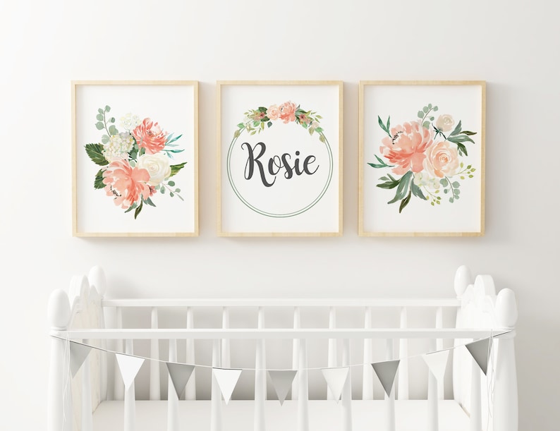 May include: Three framed prints with a floral theme. The center print features a wreath of flowers with the name "Rosie" in the center. The prints on either side feature bouquets of pink and white flowers.
