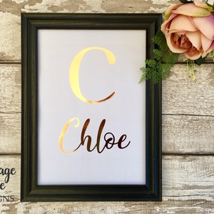 May include: A black framed print with a gold foil letter "C" and the name "Chloe" written in gold foil script.