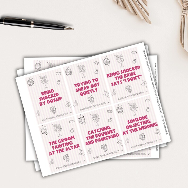 May include: A stack of pink and white cards with various phrases in black and pink text, including "Being Shocked by Gossip" and "Trying to Sneak Out Quietly." The cards have illustrations of cocktails, disco balls, and rings. A black pen is visible.