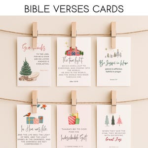 May include: Cards with Bible verses are displayed on a string with wooden clips. The cards feature illustrations of Christmas trees, a barn, and gifts. The text includes phrases like "Give Thanks" and "The True Light."