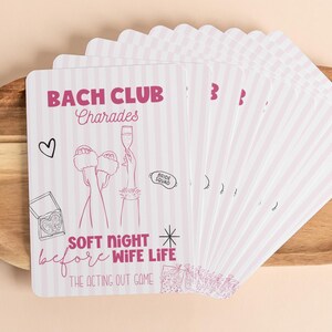May include: A stack of pink and white striped cards with the text "BACH CLUB Charades" and illustrations of a heart, champagne, and slippers. The cards also read "SOFT NIGHT before WIFE LIFE" and "THE ACTING OUT GAME".