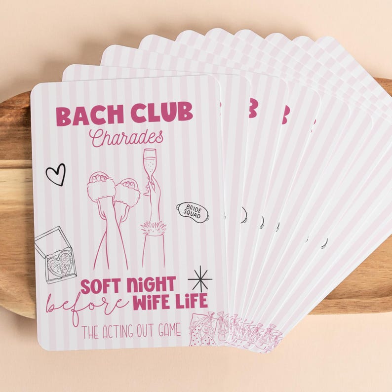 May include: A stack of pink and white striped cards with the text "BACH CLUB Charades" and illustrations of a heart, champagne, and slippers. The cards also read "SOFT NIGHT before WIFE LIFE" and "THE ACTING OUT GAME".