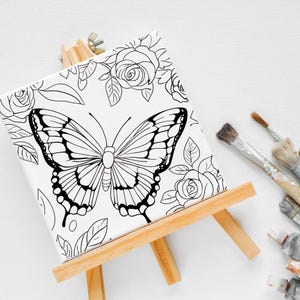 May include: A black and white line drawing of a butterfly and roses on a white canvas on an easel. The canvas is ready to be painted.