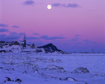 Maanlicht bij zonsopgang in de winter, op Cap-Chat, zijn dorp, het ijs, de kerk en de vuurtoren