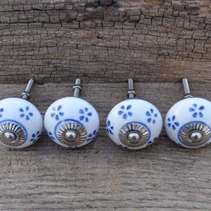 May include: Set of four white ceramic cabinet knobs with blue floral designs and silver accents.