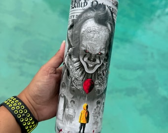 May include: A stainless steel tumbler featuring a black and white image of a scary clown with a red balloon. The tumbler also has an image of a child in a yellow raincoat. The tumbler is cylindrical and appears to be approximately 8 inches tall.