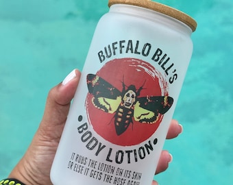 May include: A white frosted glass tumbler with a bamboo lid and a straw. The tumbler features a graphic of a red circle with a black and yellow moth with a skull on its head. The text "BUFFALO BILL'S BODY LOTION" is printed on the tumbler. The text "IT RUBS THE LOTION ON ITS SKIN OR ELSE IT GETS THE HOSE AGAIN" is printed below the graphic.