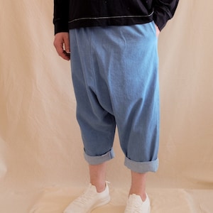 Può includere: Una persona che indossa una maglietta nera a maniche lunghe con un segno di pace bianco ricamato sul davanti, pantaloni di jeans blu con orlo arrotolato e scarpe da ginnastica bianche.