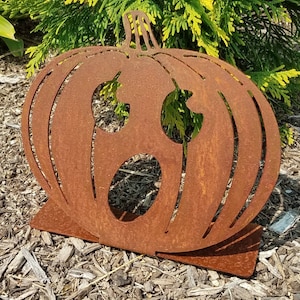 May include: A rusty metal pumpkin with a carved out face. The pumpkin is standing on a small base and has a distressed look.