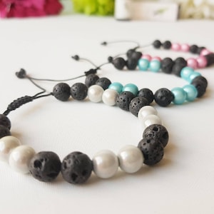 May include: Three adjustable bracelets with black lava rock beads and white pearl beads. The bracelets are strung on black cord.