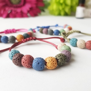 Puede incluir: Un conjunto de pulseras de piedra de lava de colores con cierres ajustables de cuerda. Las pulseras presentan cuentas redondas y porosas en tonos de rojo, naranja, amarillo, verde, azul y morado.