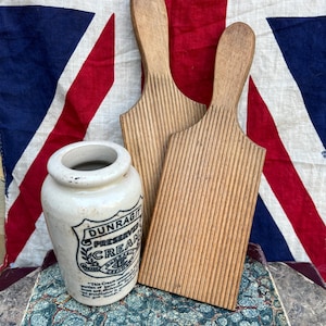May include: Two wooden butter paddles with vertical ribbed textures and a cream-colored ceramic jar featuring the black text "DUNRAGIT PRESERVED CREAM" and a decorative shield emblem, all arranged together as a set of kitchen items.