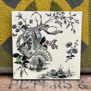 Puede incluir: Azulejo cerámico cuadrado con fondo crema e ilustración detallada en blanco y negro. El diseño incluye un pájaro, flores, un velero y otros elementos decorativos. El azulejo es probablemente para uso decorativo.