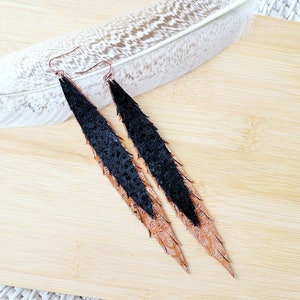 May include: A pair of long, black and brown leather earrings with a feather-like design. The earrings are hanging on a wooden surface.