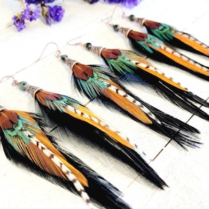May include: A pair of long, colourful feather earrings with copper wire and beads. The feathers are black, orange, teal, and brown.