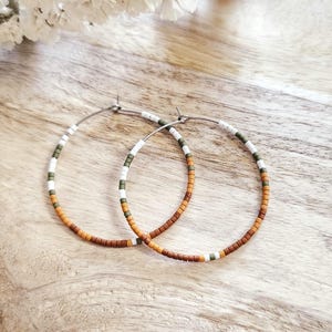 May include: A pair of hoop earrings with brown, white, and green beads. The earrings are made of metal and have a simple, minimalist design.