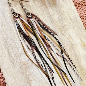 May include: A pair of long, colorful feather earrings with brown, white, and black feathers. The earrings have a silver bead at the top and a hook closure.