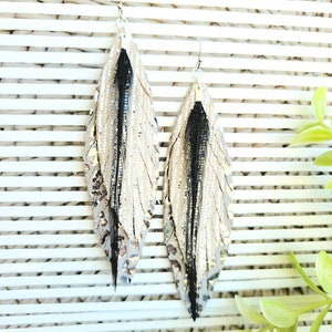 May include: A pair of long, silver feather earrings with black feathers. The earrings are made of leather and have a metallic finish.
