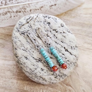 May include: Turquoise and orange beaded earrings with silver-tone metal accents. The earrings feature a rectangular link design and are displayed on a textured stone surface.