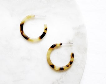 May include: A pair of brown and cream colored hoop earrings. The earrings are made of a tortoiseshell-like material.