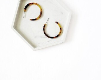 May include: Two tortoise shell hoop earrings on a white marble tray.