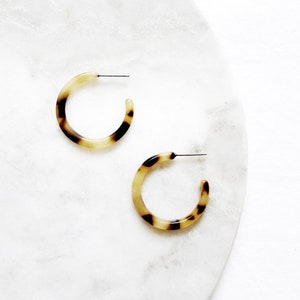 May include: A pair of brown and cream hoop earrings. The earrings are made of a tortoiseshell-like material.