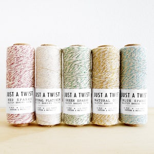 May include: Five spools of twine with different colored glitter threads. The twine is labeled "Just a Twist" and the colors are red, white, green, gold, and blue.