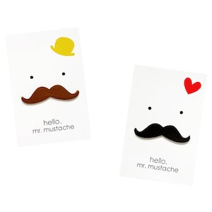Peut inclure: Deux cartes blanches avec un visage de dessin animé sur chacune. Le visage sur la carte de gauche a une moustache brune, un chapeau jaune et le texte "hello, mr. mustache". Le visage sur la carte de droite a une moustache noire, un cœur rouge et le texte "hello, mr. mustache".
