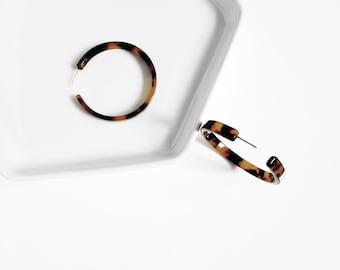 May include: A pair of brown and black tortoise shell hoop earrings. The earrings are made of plastic and have a shiny finish.