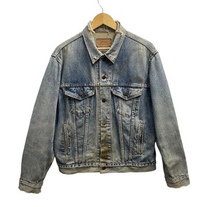Könnte beinhalten: Eine hellblaue Jeansjacke mit verwaschener Optik. Sie verfügt über einen spitzen Kragen, eine Knopfleiste vorne, zwei Brusttaschen mit geknöpften Klappen und zwei vertikale Seitentaschen. Ein kleines rotes Etikett ist an der Tasche sichtbar.