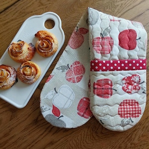 Puede incluir: Un guante de cocina con un diseño de manzanas rojas y una bandeja para servir con pasteles horneados. El guante presenta un detalle de lunares rojos y detalles acolchados. Los pasteles son dorados y espolvoreados con azúcar en polvo.