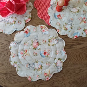 Peut inclure: Un ensemble de trois sets de table matelassés beiges avec un bord festonné. Les sets de table présentent un motif répétitif de lapins, de fleurs et d'œufs.