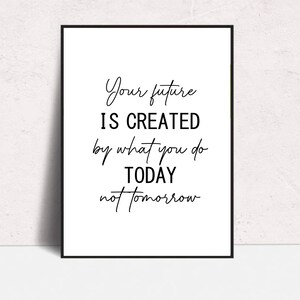 Puede incluir: Impresión enmarcada con fondo blanco y texto negro. El texto dice "Your future is created by what you do TODAY not tomorrow" en un estilo manuscrito. El marco es negro.