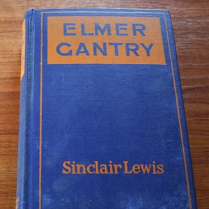 May include: A blue hardcover book with the title "Elmer Gantry" in orange lettering on the spine. The author, Sinclair Lewis, is printed in orange lettering below the title.