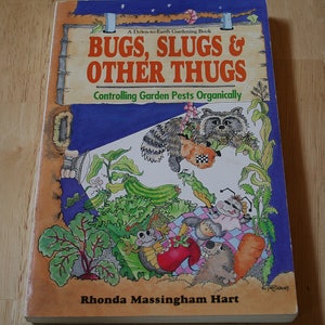 May include: Book cover with a blue background and a cartoon raccoon holding a bag of garden pests. The title is "Bugs, Slugs & Other Thugs: Controlling Garden Pests Organically" by Rhonda Massingham Hart.