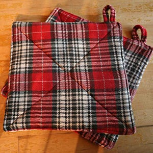 May include: Two red and white plaid pot holders with black trim. The pot holders are folded in half and have a quilted design.