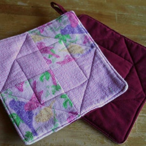 May include: Two pot holders, one with a floral pattern in shades of pink, purple, and white, and the other a solid burgundy color.