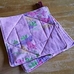 May include: Purple and pink quilted hot pad with a floral pattern. The hot pad has a burgundy loop for hanging.