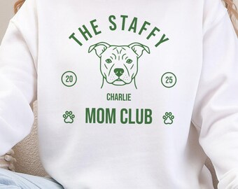 May include: White crew neck sweatshirt featuring a green graphic with the text "The Staffy Mom Club" and a dog illustration. The design includes paw prints and the name "Charlie".