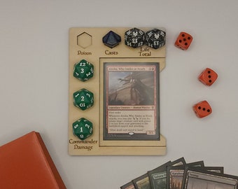 Könnte beinhalten: Ein Kartenhalter aus Holz mit Schlitzen für Würfel und eine Magic: The Gathering-Karte. Der Halter hat Textbeschriftungen für "Poison", "Casts", "Life Total" und "Commander Damage". Grüne, schwarze und orangefarbene Würfel sind verstreut.