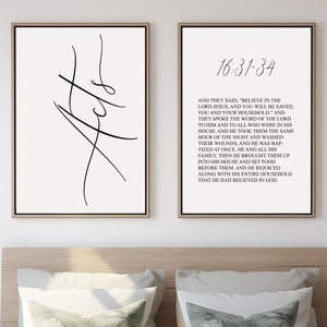 May include: Two black and white prints with a minimalist design. The left print features the word "Acts" in a stylized font. The right print features a Bible verse from Acts 16:31-34. The prints are displayed on a white wall above a bed with a white duvet and two green pillows.