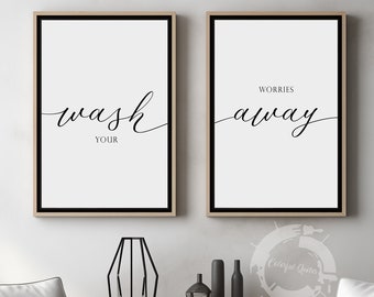 May include: Two framed prints with black calligraphy on a white background. The left print says "Wash Your" and the right print says "Worries Away". The prints are hanging on a white wall above a wooden table with two white chairs.