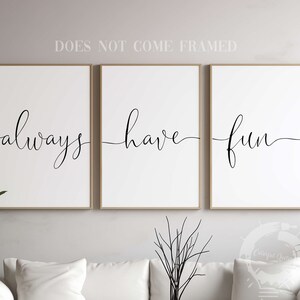 Könnte beinhalten: Drei Schwarzweißdrucke mit den Worten "always", "have" und "fun" in einer kursivschriftlichen Schriftart. Die Drucke sind in einem hellen Holzrahmen gerahmt und hängen an einer hellgrauen Wand.