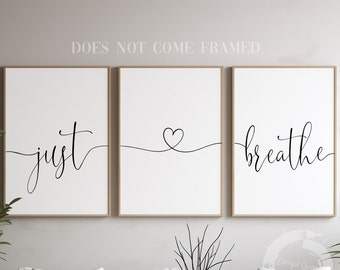 May include: Three framed prints with the words "just", a heart, and "breathe" in a modern calligraphy style. The prints are hung on a light gray wall above a white couch.