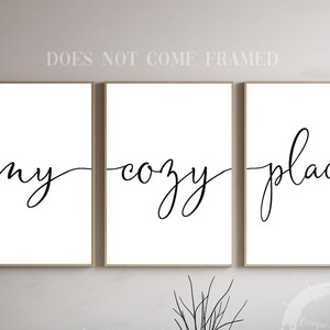 Könnte beinhalten: Drei gerahmte Kunstdrucke mit den Worten "my cozy place" in eleganter schwarzer Schrift auf weißem Hintergrund. Die Rahmen sind hellbraun. Der Satz ist auf die drei Drucke aufgeteilt.