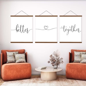 K&ouml;nnte beinhalten: Drei gerahmte Drucke mit den Worten "better", einem Herzsymbol und "together" in schwarzer Kalligraphie auf wei&szlig;em Hintergrund. Die Drucke h&auml;ngen an einer wei&szlig;en Wand &uuml;ber zwei orangen Sesseln mit gemusterten Kissen.