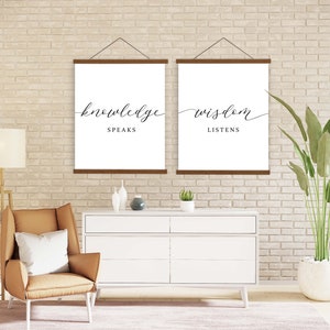 K&ouml;nnte beinhalten: Zwei gerahmte Drucke mit dem Text "knowledge speaks" und "wisdom listens" h&auml;ngen an einer Backsteinwand. Die Drucke sind in Schwarzwei&szlig; gehalten und haben ein schlichtes, modernes Design.
