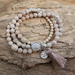 May include: A triple-strand bracelet with light pink and white beads, silver accents, and a silver charm with a floral design. The bracelet has a light brown tassel.