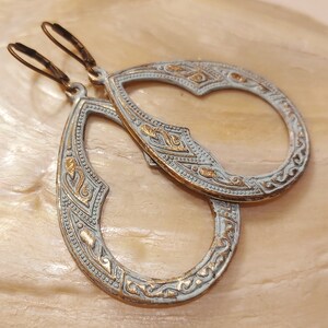 May include: A pair of silver and gold teardrop-shaped earrings with intricate filigree designs. The earrings have a distressed finish and are perfect for adding a touch of bohemian style to any outfit.